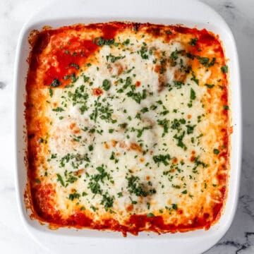 Overhead view of finished chicken mozzarella in white baking dish topped with parsley.