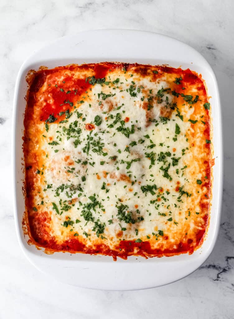 Overhead view of finished chicken mozzarella in white baking dish topped with parsley.