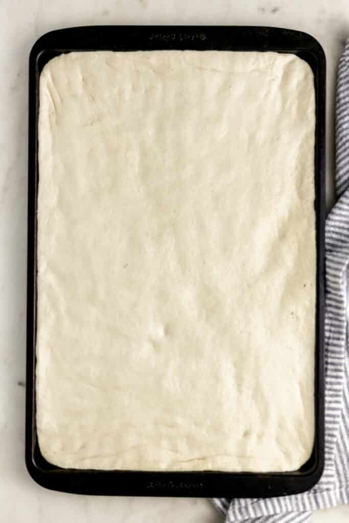 pizza dough rolled out into square baking sheet with napkin