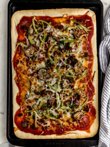 overhead view supreme pizza in square baking sheet with napkin and pizza cutter