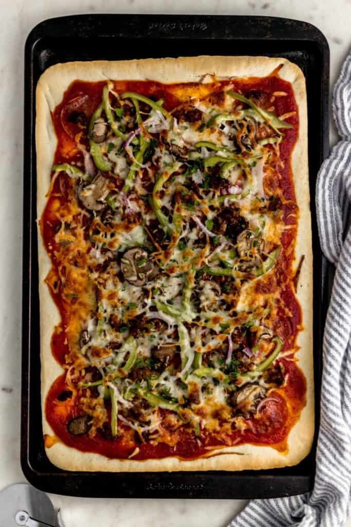 overhead view supreme pizza in square baking sheet with napkin and pizza cutter