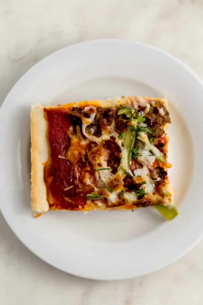 square piece of supreme pizza on white plate 