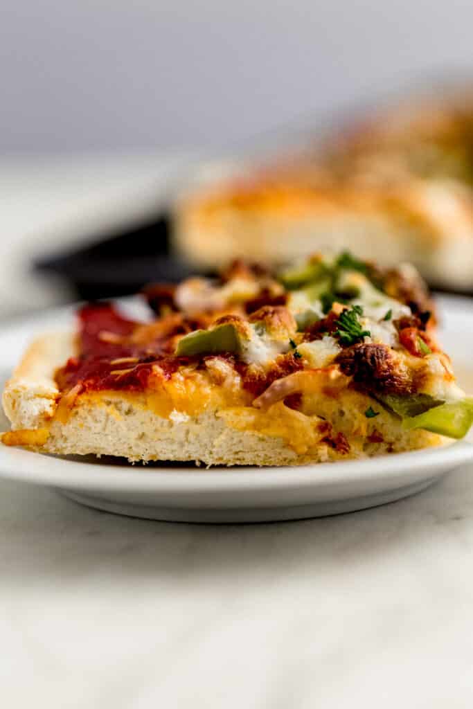 close up side view supreme pizza piece on small white plate 