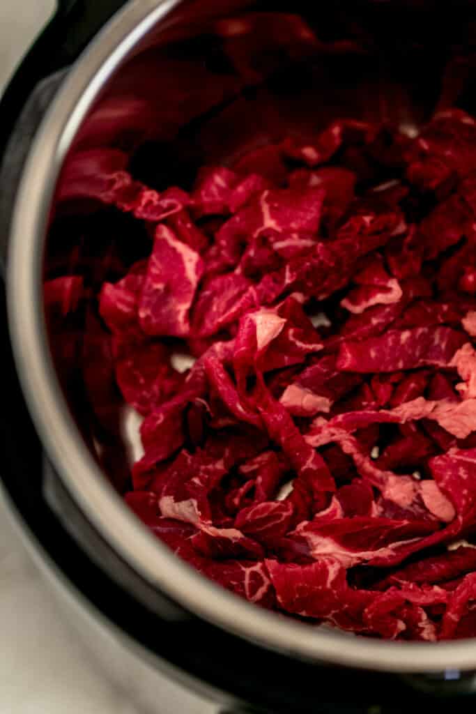thinly sliced steak in bottom of the instant pot pressure cooker 