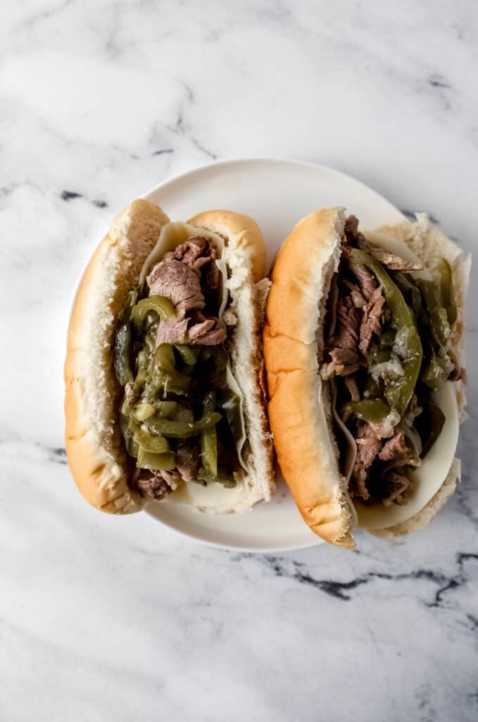 overhead view of two finished cheesesteaks on a white plate on a marble surface