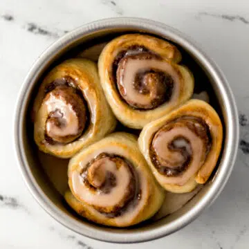 silver baking pan with four cinnamon rolls topped with icing in it