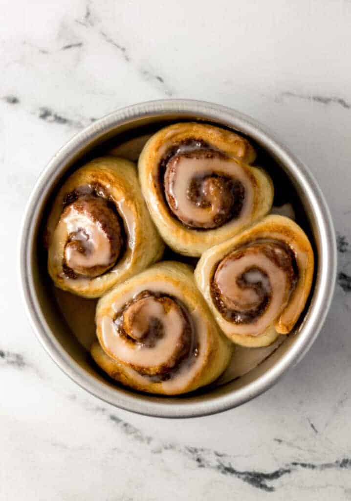 silver baking pan with four cinnamon rolls topped with icing in it