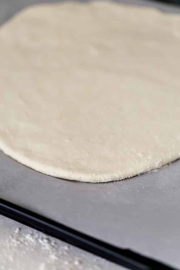 side view pizza dough on parchment lined baking pan 