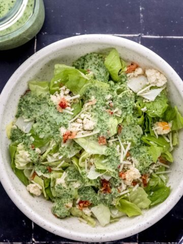 Overhead view of salad in white bowl beside a fork and jar of dressing.