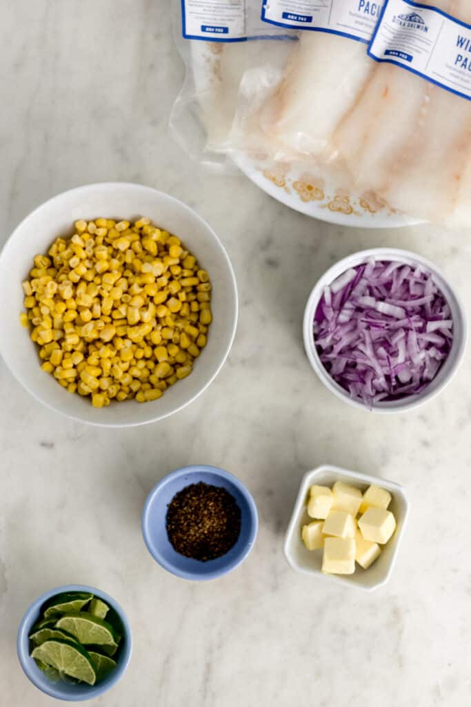 ingredients for cod in parchment recipe in small bowls and a plate on marble base 