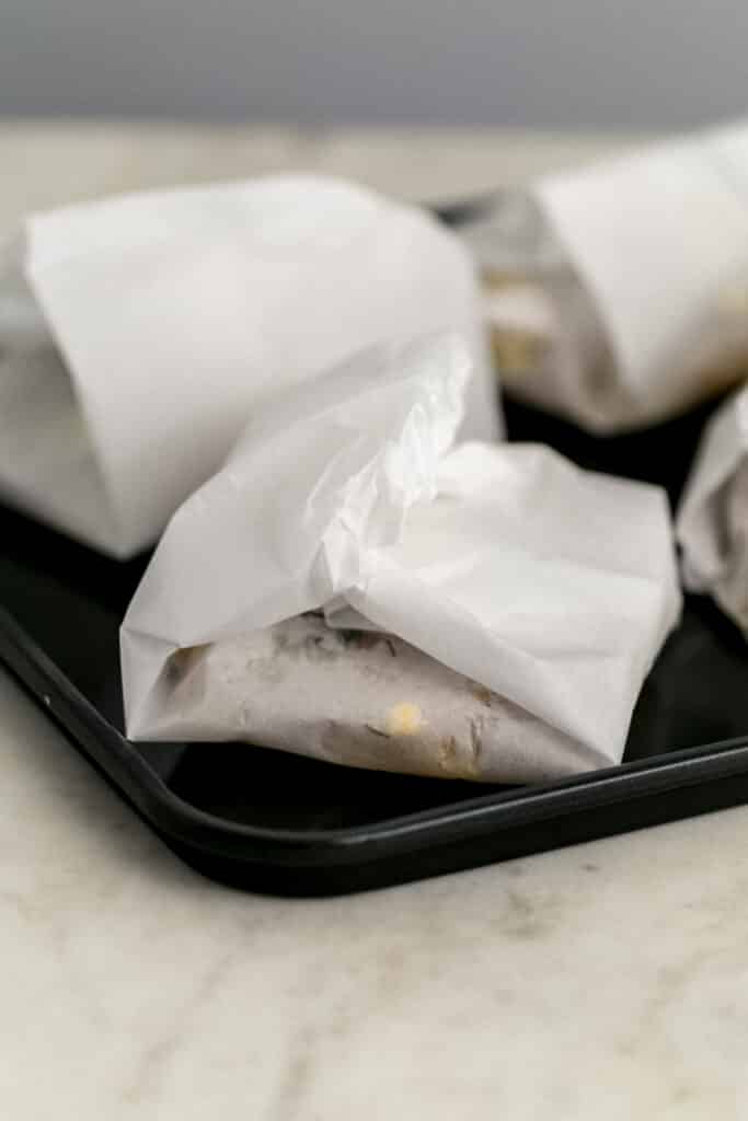 cod wrapped in parchment paper on baking sheet before baking