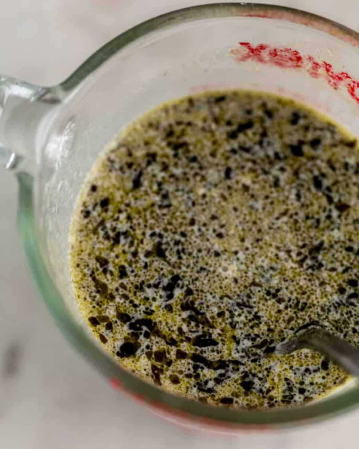 Pesto sauce ingredients combined in glass measuring cup.