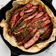 Overhead view of finished steak topped with parsley in parchment lined cast iron skillet.
