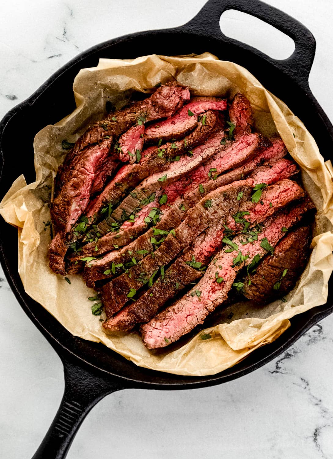 Overhead view of sliced flank steak in cast iron topped with parsley.