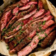 Close up overhead view of sliced steak topped with parsley in parchment lined skillet.