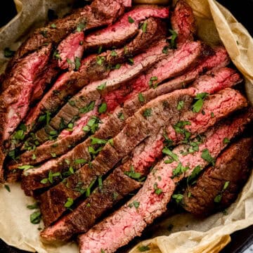 Close up overhead view of sliced steak topped with parsley in parchment lined skillet.