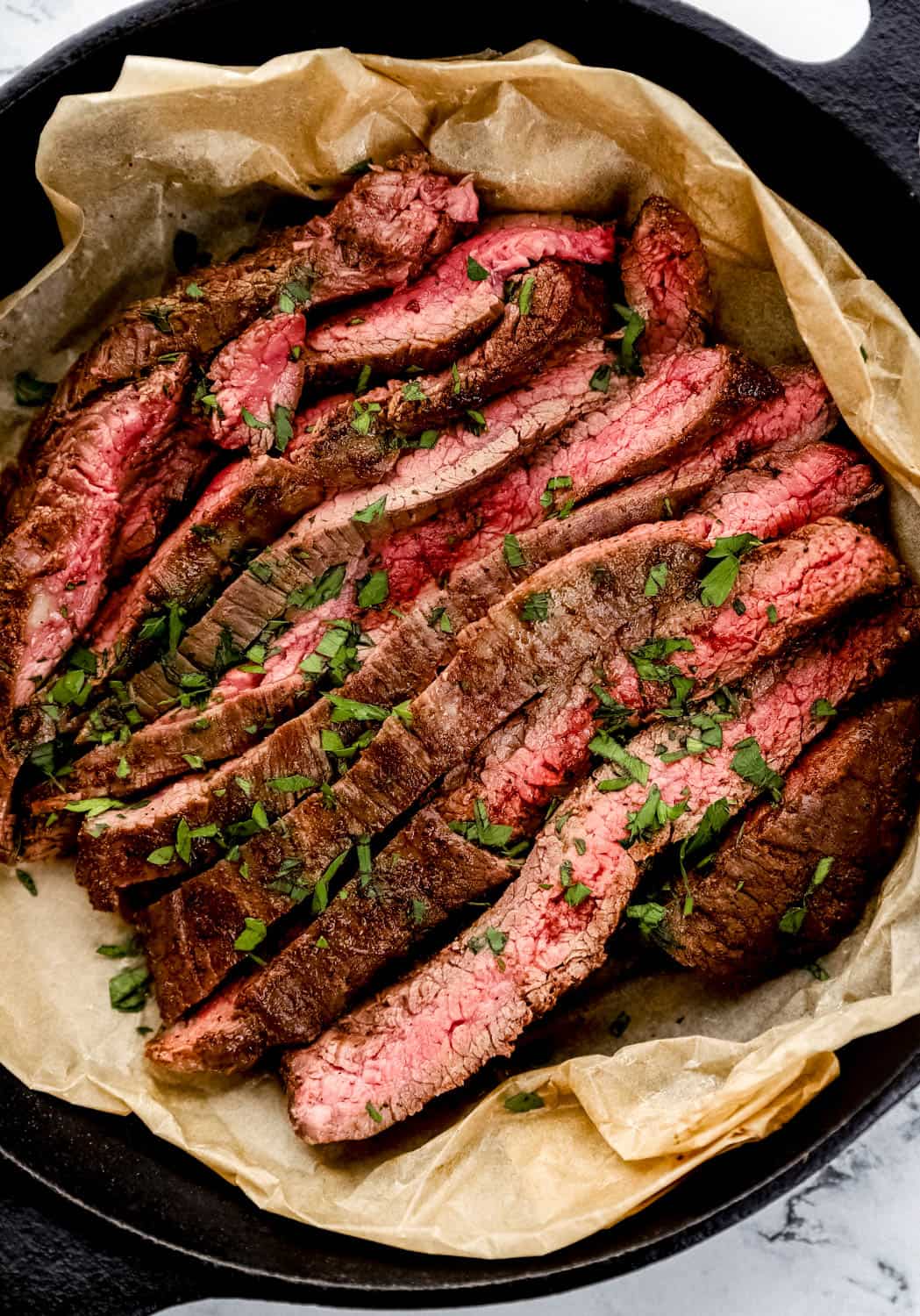 Overhead view of sliced steak on top of parchment paper in cast iron skillet.