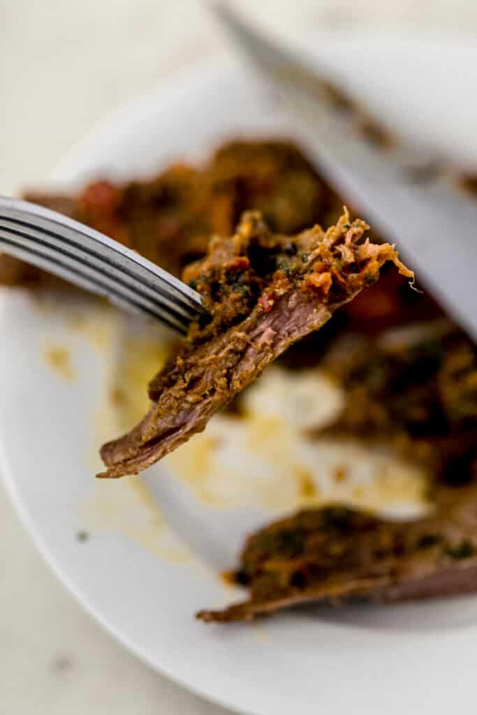 hand holding fork with flank steak and pesto on it over white plate with more steak on it