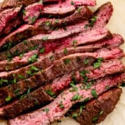 Close up view of sliced steak topped with parsley on parchment paper.