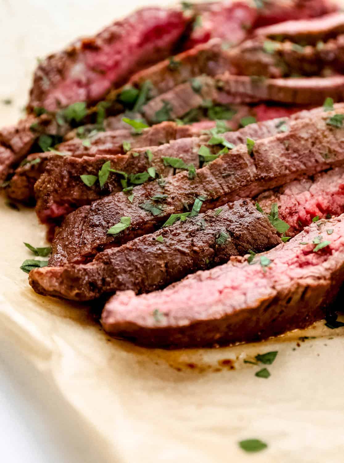 Close up front view of parsley topped sliced steak on parchment paper.