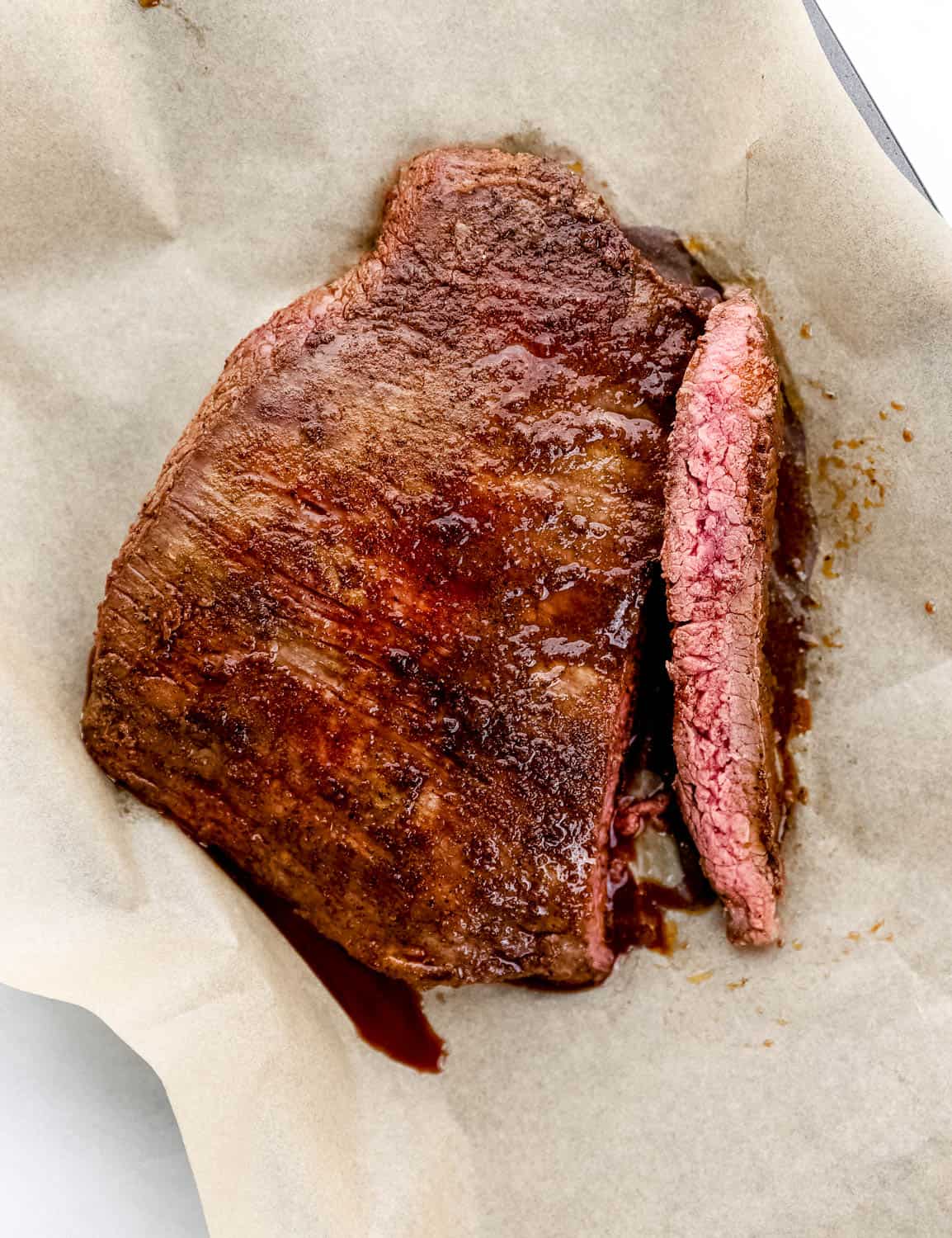 Overhead view of finished flank steak on top of parchment paper on sheet pan.