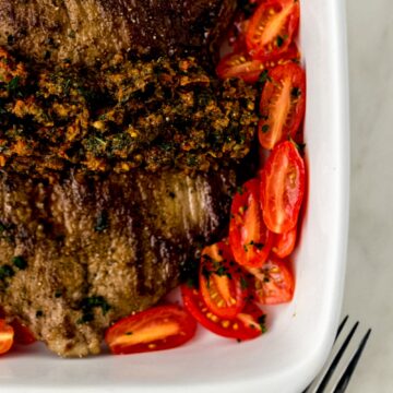 flank steak in square white baking dish topped with sun dried tomato pesto