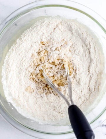 Wet and dry ingredients in glass mixing bowl with whisk.
