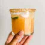 hand holding glass with kombucha margarita in it and lime wedge.