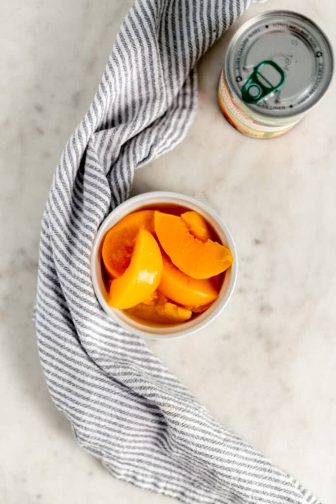 small white bowl with sliced cling peaches next to can of peaches