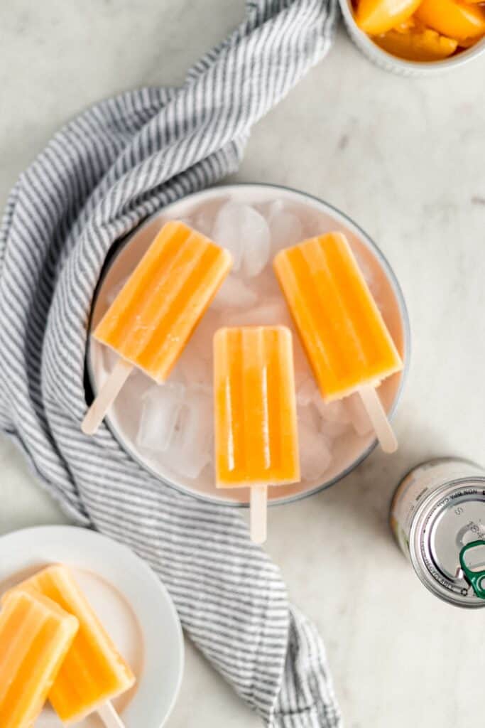 serving bowl with three popsicles on it over ice, white plate with additional popsicles, cloth napkin 