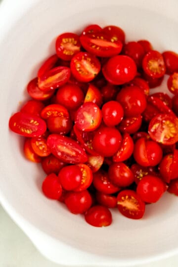 Overhead view of halved tomatoes in mixing bowl.