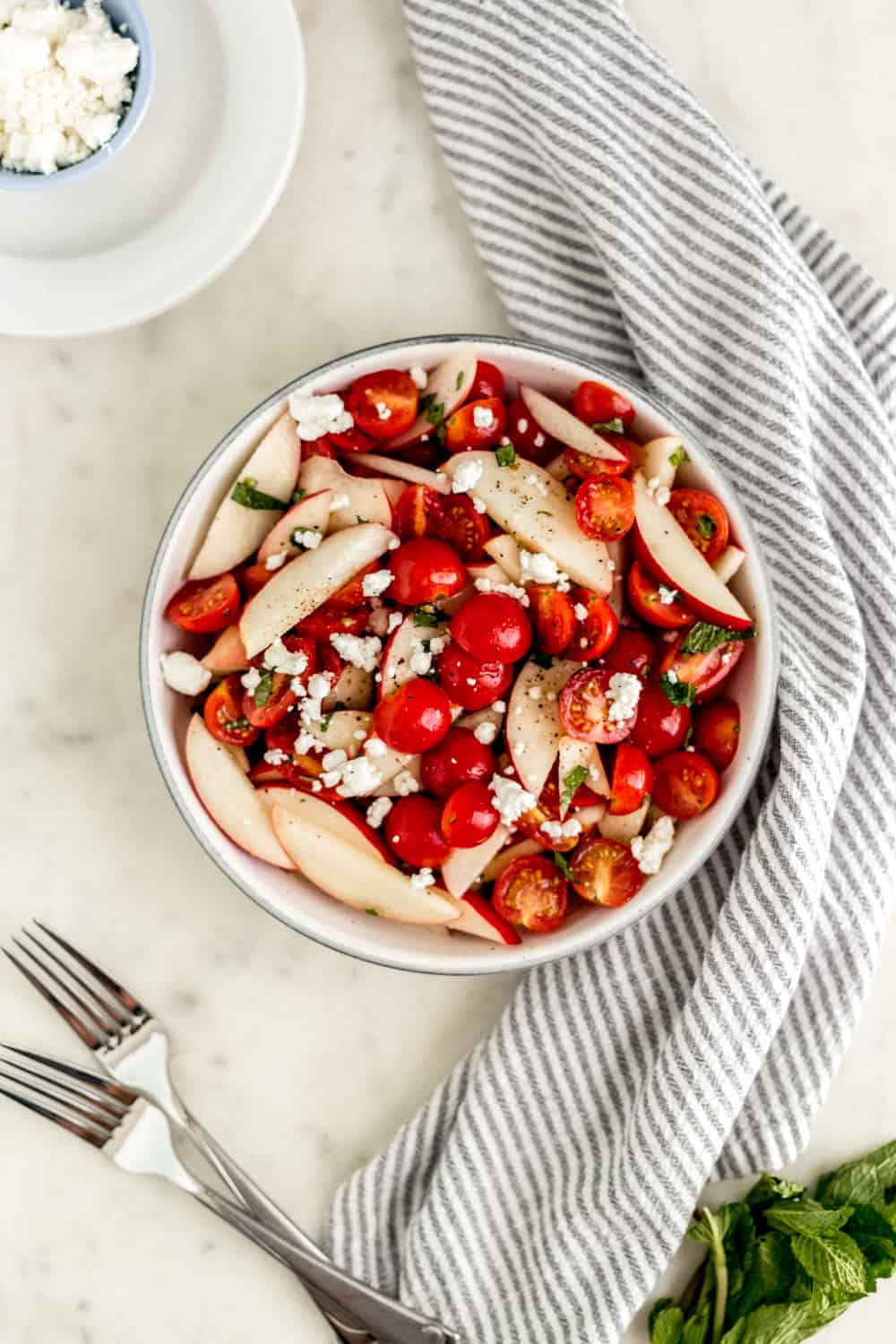 Overhead view of finished tomato peach salad in a bowl by napkin and forks.