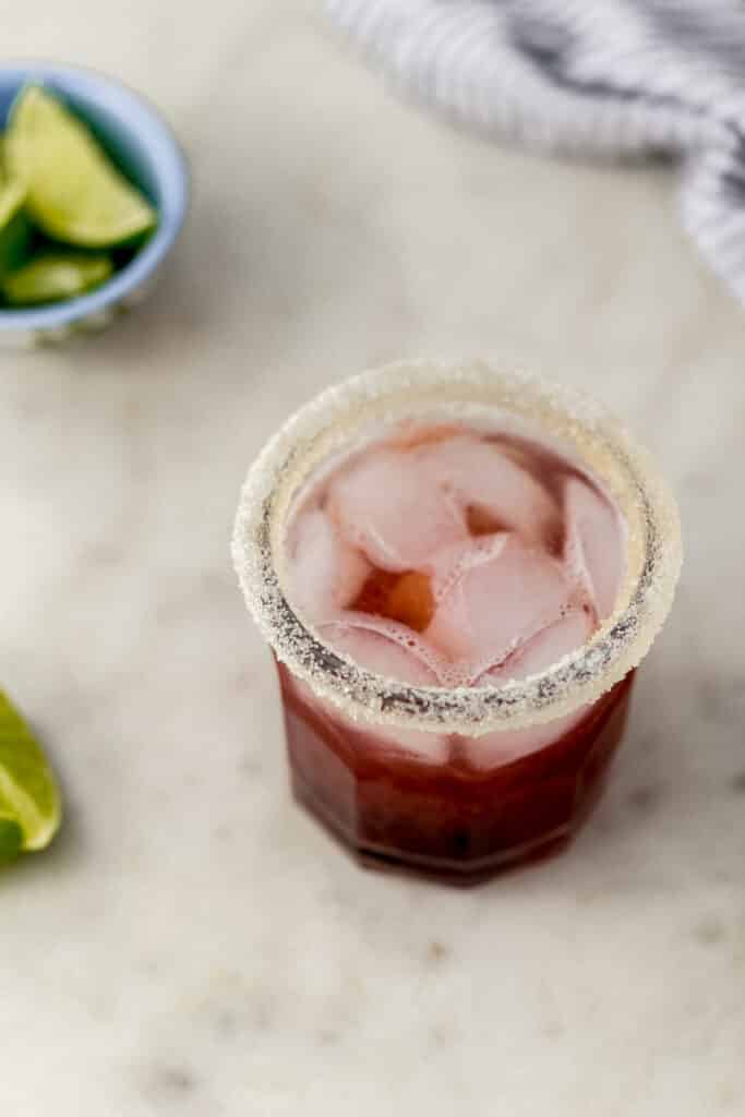 side view cherry margarita in sugar rimmed glass with ice and limes on the side 