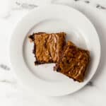 overhead view of two brownies on small white plate on marble surface