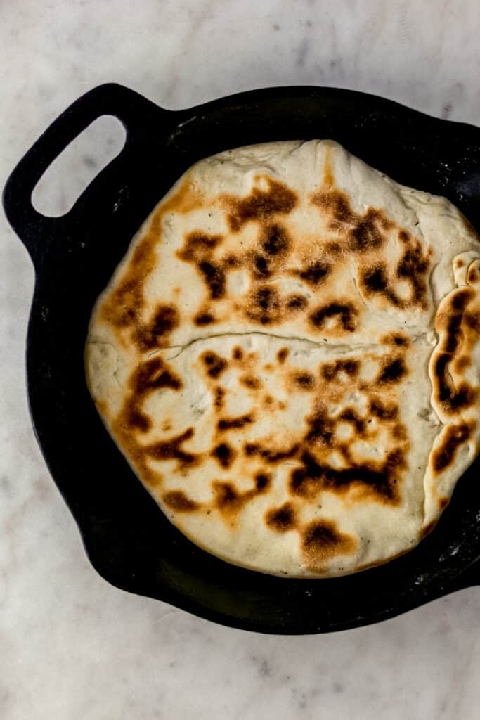 pizza dough in cast iron skillet after cooking on one side