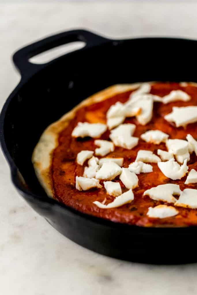Pizza crust topped with tomato sauce and mozzarella cheese in cast iron skillet 