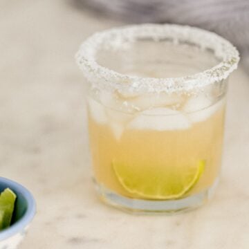 close up side view margarita in salt rimmed glass with small bowl of lime wedges