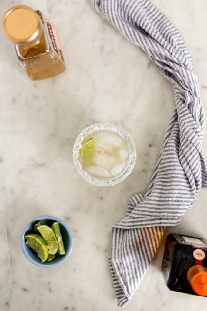 overhead view of margarita in a glass rimmed with salt with bottles, limes, and cloth napkin