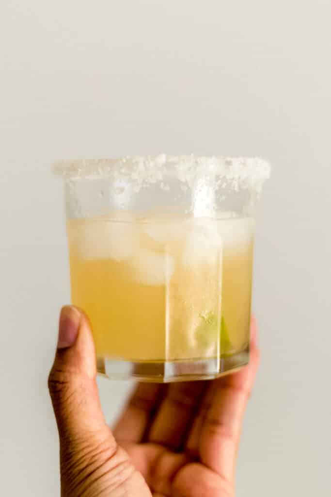 hand holding salt rimmed glass with margarita in it.