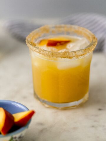 margarita in glass beside a small bowl of peach slices