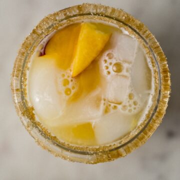 sugar rimmed glass with peach margarita on ice.