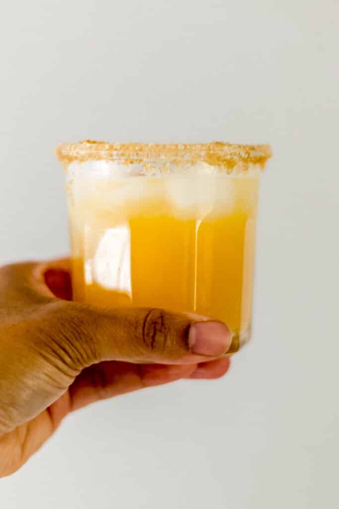 hand holding glass with peach margarita in it. 