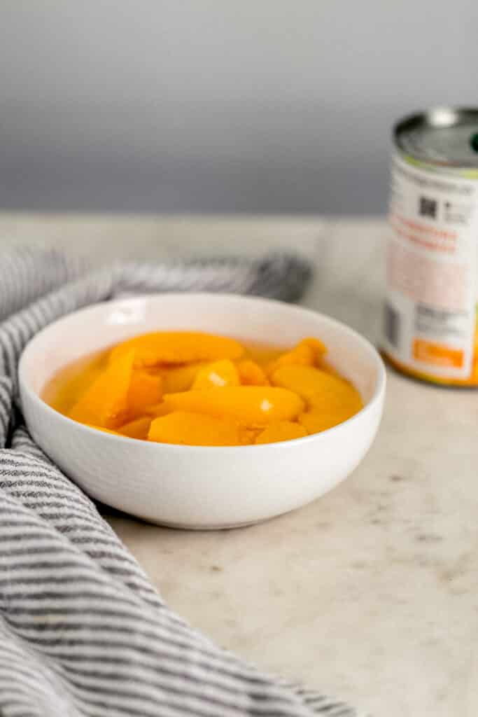 close up side view peaches in a white bowl with can of peaches next to it. 