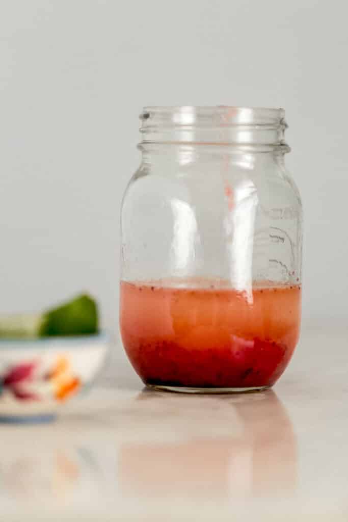 close up side view of ingredients for strawberry margarita in glass jar 