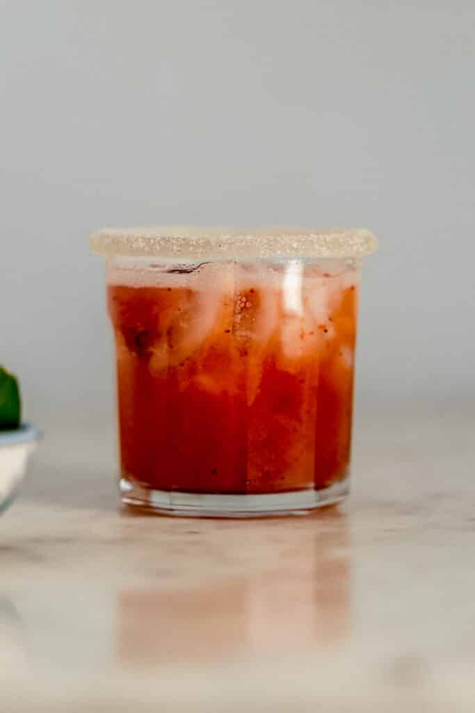 close up side view strawberry margarita in sugar rimmed glass next to small bowl with lime wedges 