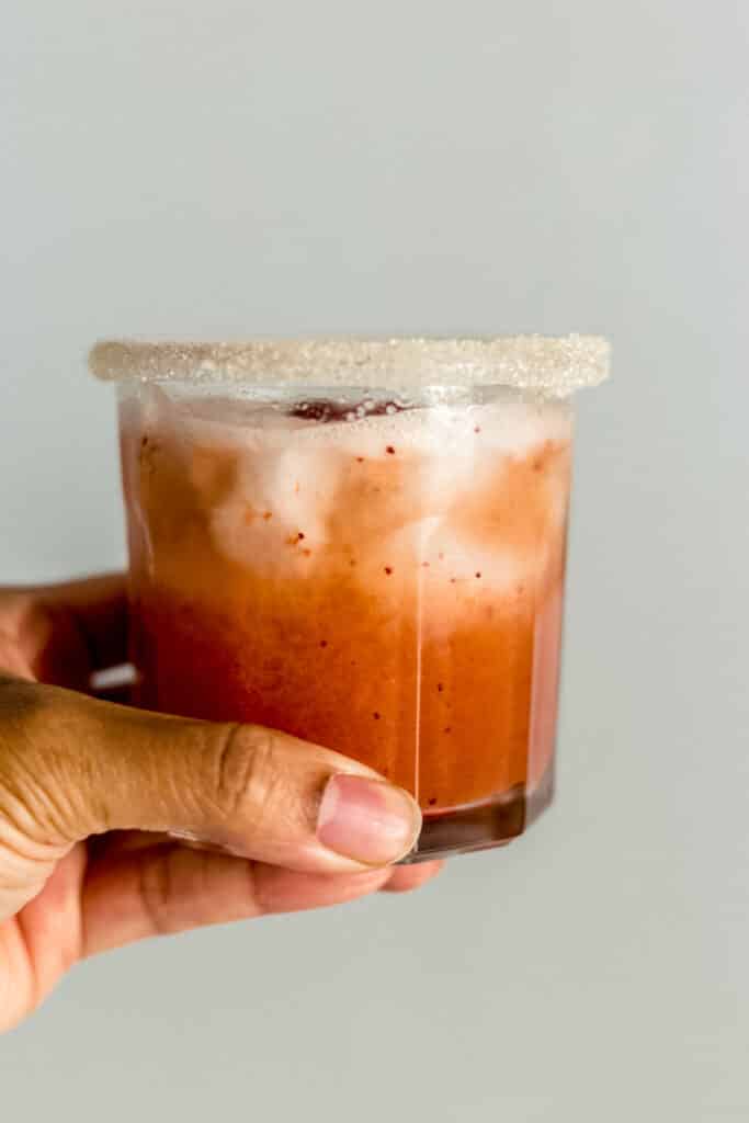 hand holding glass with strawberry margarita over ice in it. 