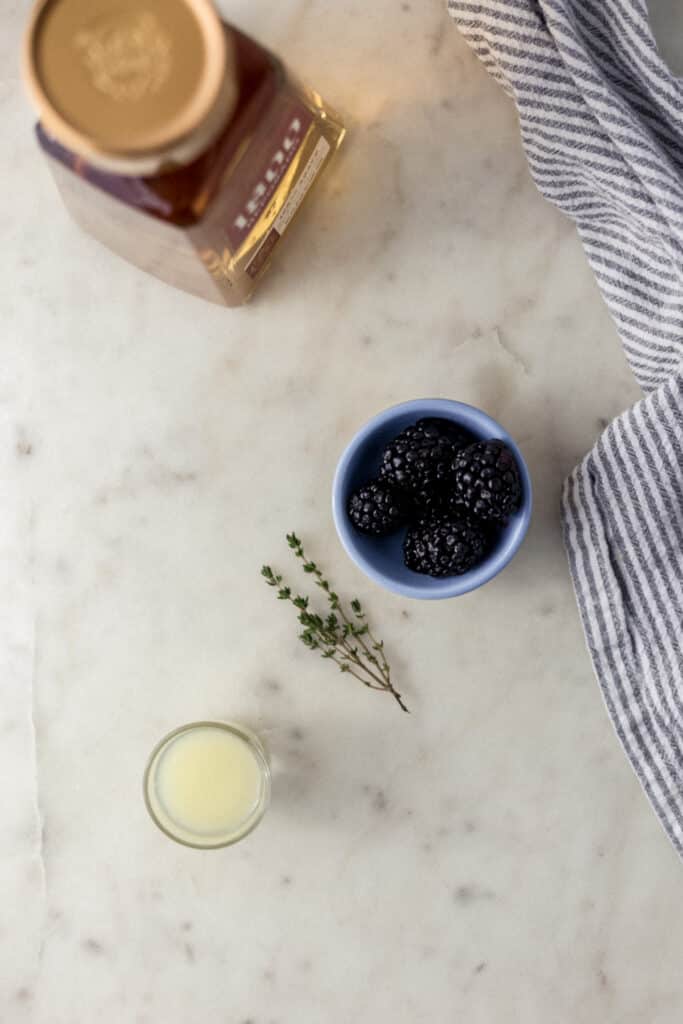 ingredients for blackberry thyme margarita with cloth napkin on marble surface 