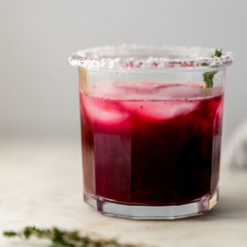 close up side view of glass with blackberry margarita on ice in it.