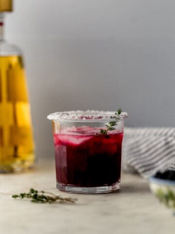 close up side view blackberry thyme margarita in salt rimmed glass with ice