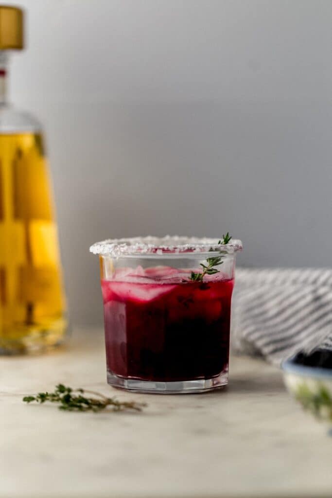 close up side view blackberry thyme margarita in salt rimmed glass with ice 